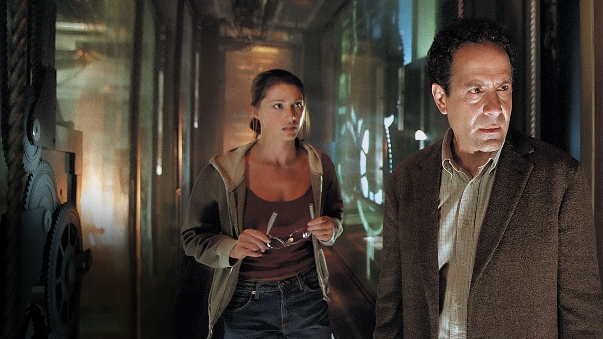 Screenshot from the film Thirt13en Ghosts. A man and a woman stand in a dark hallway near machinery. 