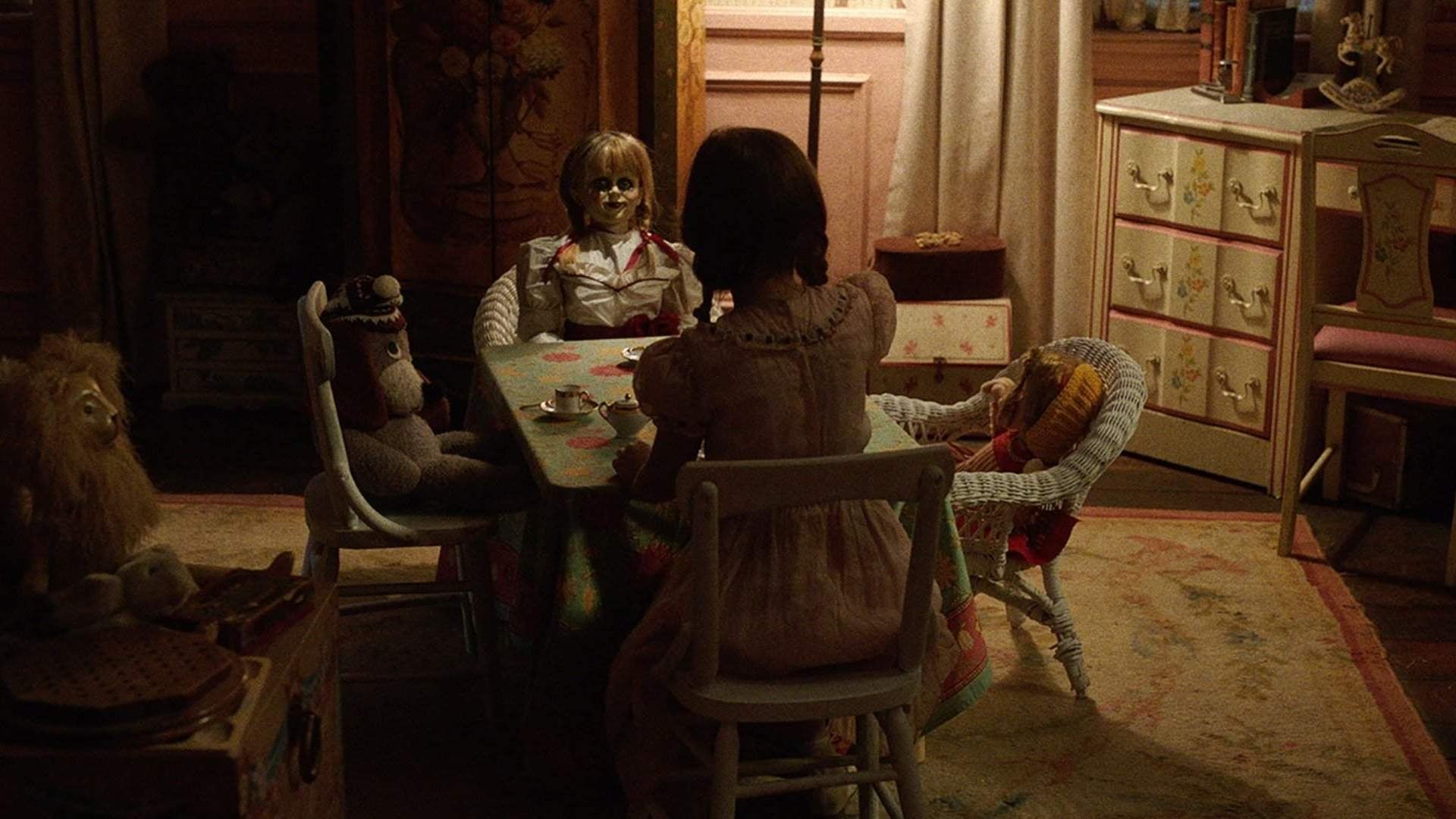 Screenshot from the film Annabelle: Creation. A young girl has a tea party with a stuffed dog, a doll, and a sinister looking doll.