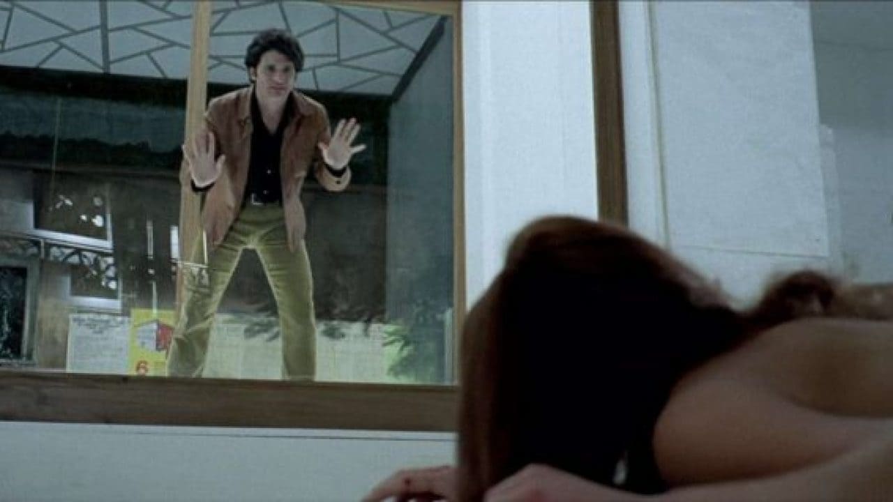 Screenshot from the film The Bird with the Crystal Plumage. A man looks through the glass at a woman lying topless on the ground.