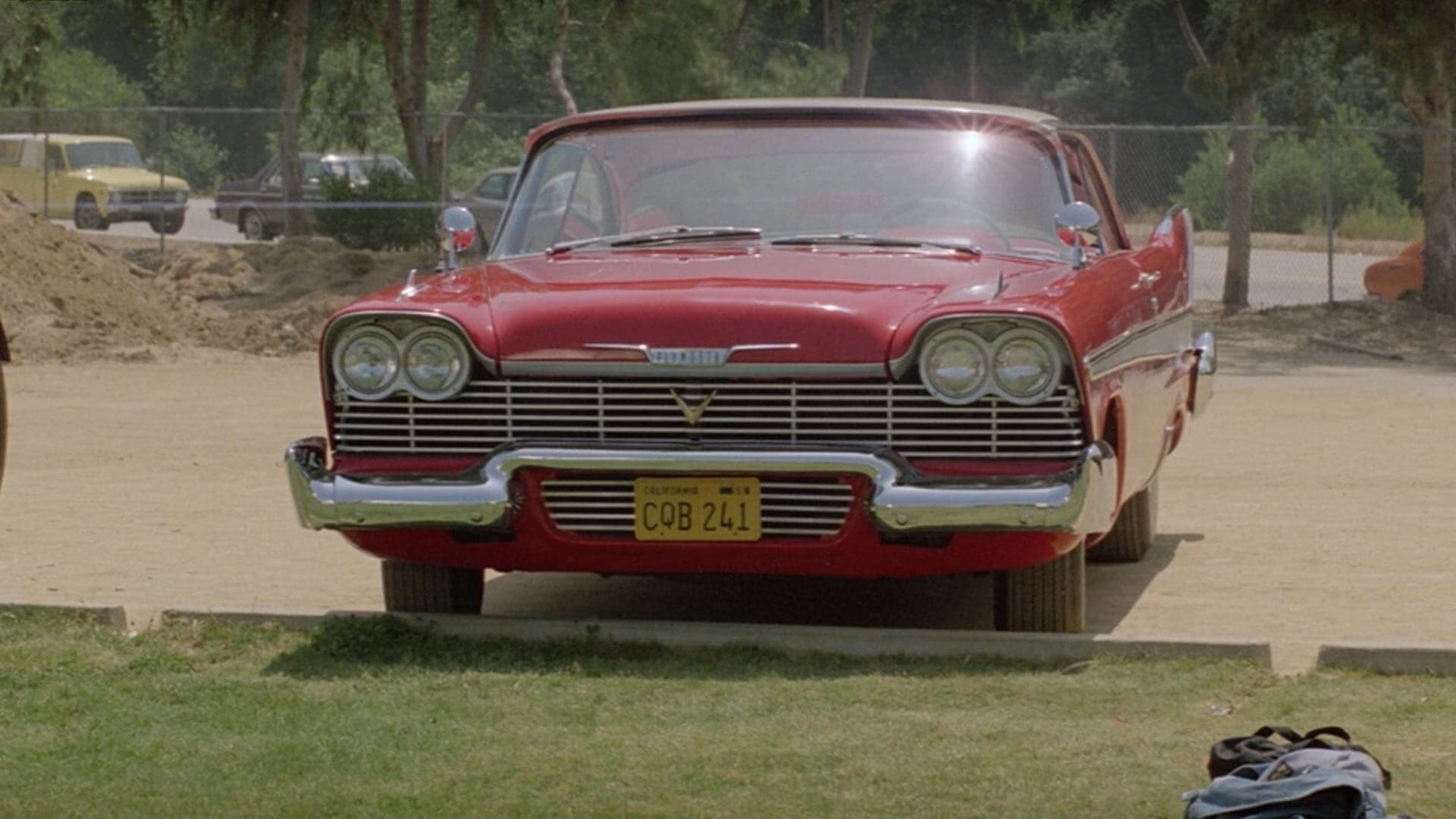 Screenshot from the film Christine. A shiny red 1958 Plymouth Fury sits in a parking lot.