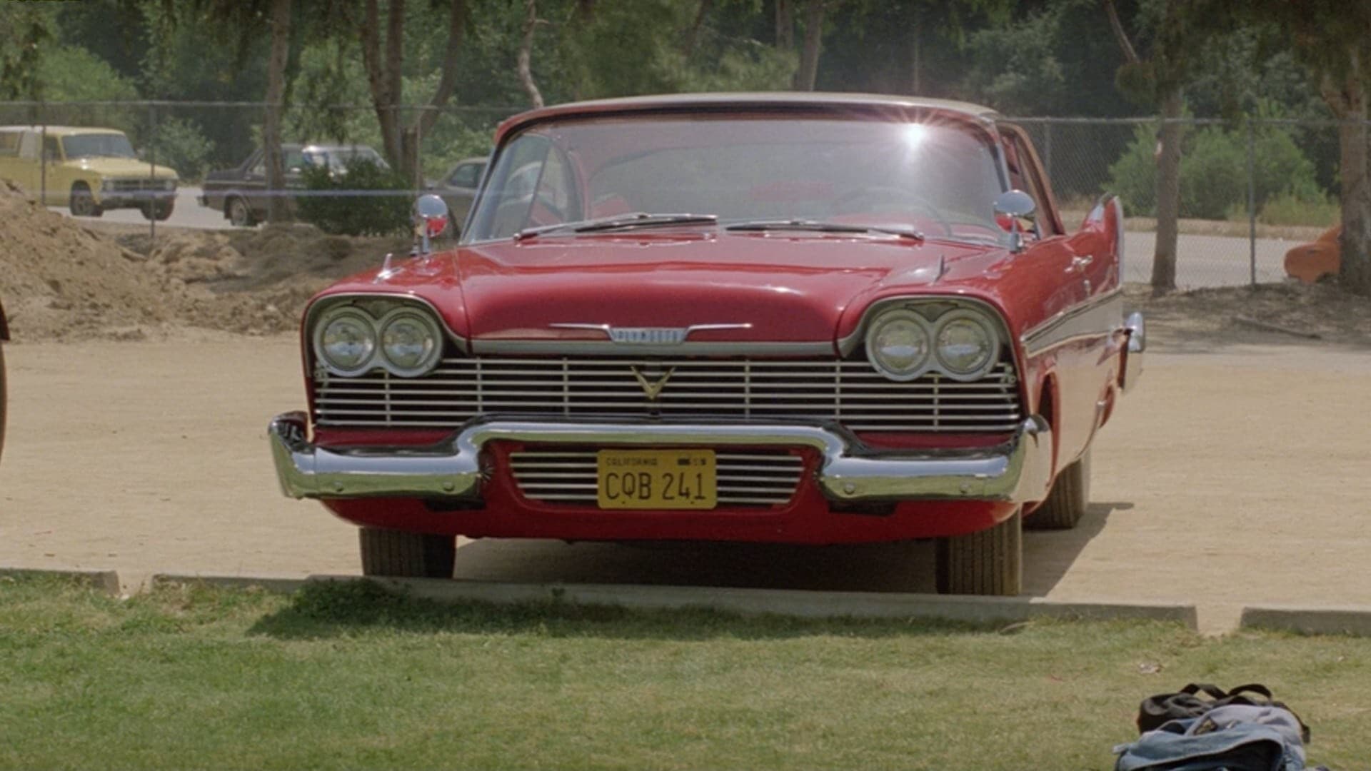 Screenshot from the film Christine. A shiny red 1958 Plymouth Fury sits in a parking lot.
