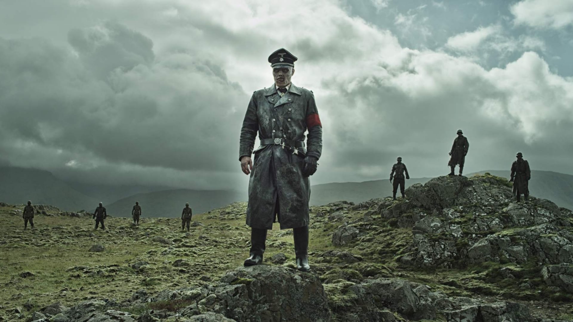 Screenshot from the film Dead Snow 2: Red vs. Dead. A zombie in a Nazi uniform stands in front of seven other zombies on a rocky terrain. 