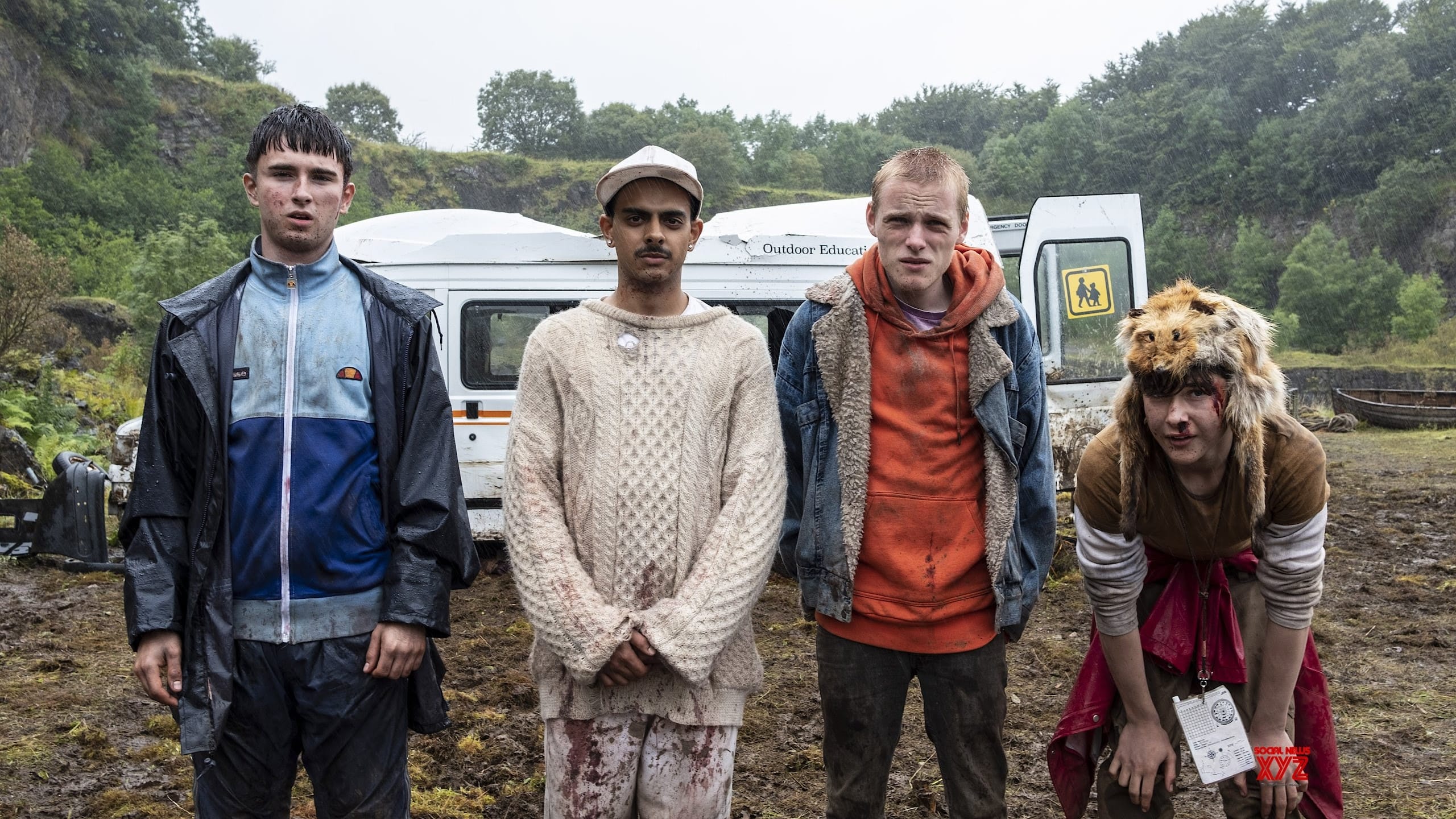 Screenshot from the film Get Duked! A group of young teens stand in the rain with their clothes wet and muddy in front of a busted van. 