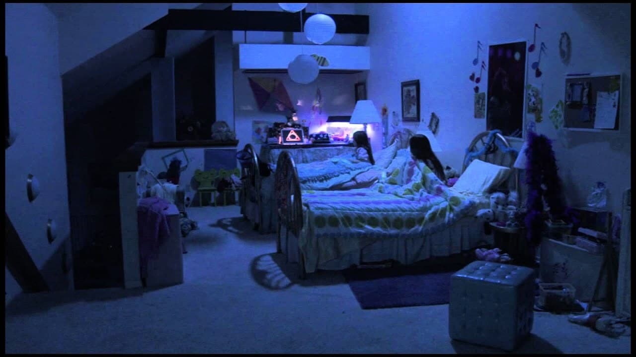 Screenshot from Paranormal Activity 3. Found footage photo of two young girls in their bedroom staring a screen with an ominous triangle image. 