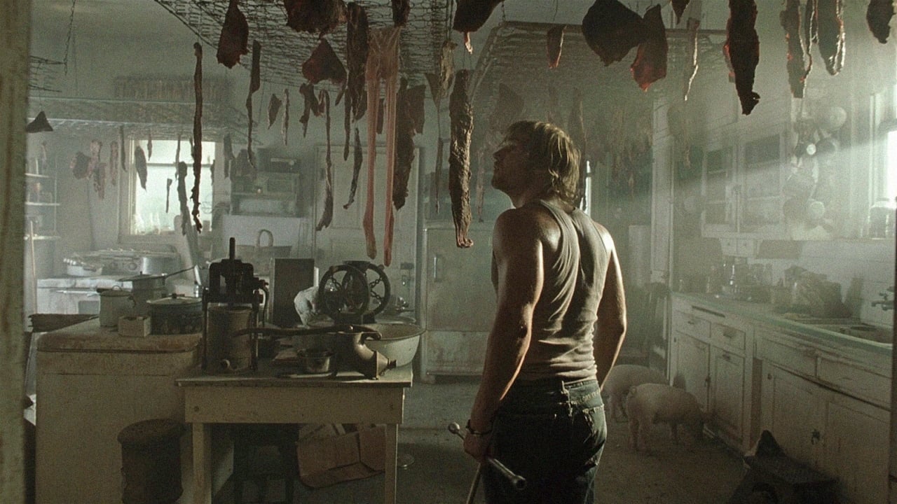 Screenshot from the 2003 film The Texas Chainsaw Massacre. A young man in a white tank top enters a kitchen with slabs a meat hanging from the ceiling. 