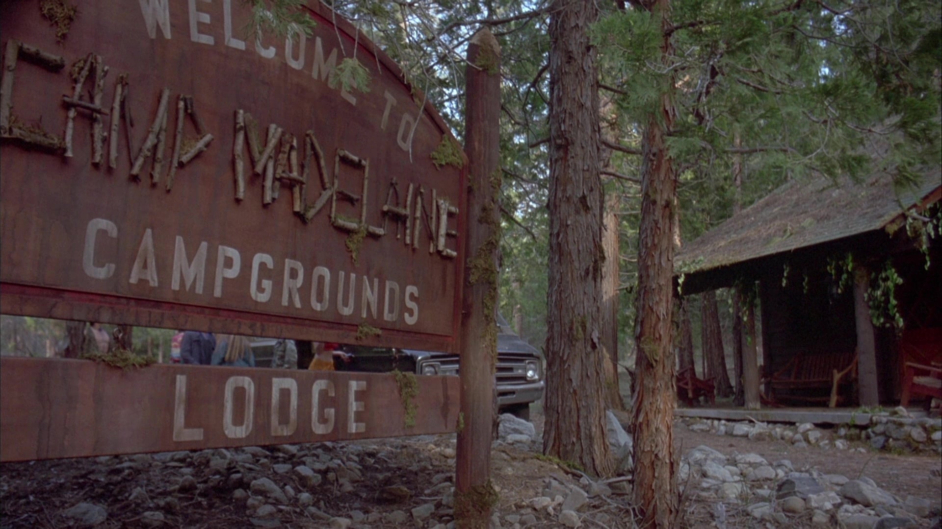 Screenshot from the film Ticks. A camp sign saying "Welcome to Camp Madelane Campgrounds Lodge"